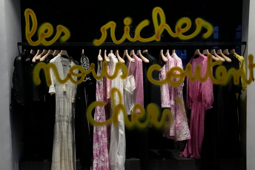 A graffiti reads "wealthy people cost us a lot" on a shop window, during a protest, Friday, April 14, 2023 in Paris.
