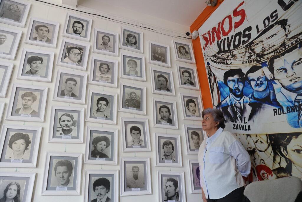 Bertha Oliva posing in front of the photos of some of the 200 detained and disappeared.Michael Fox/ Under the Shadow