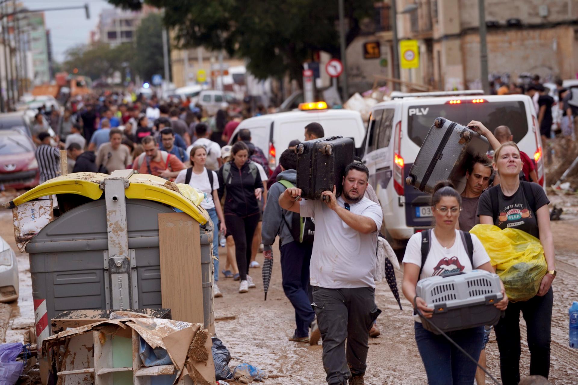 Residents carrying belongings through a muddy, flooded street