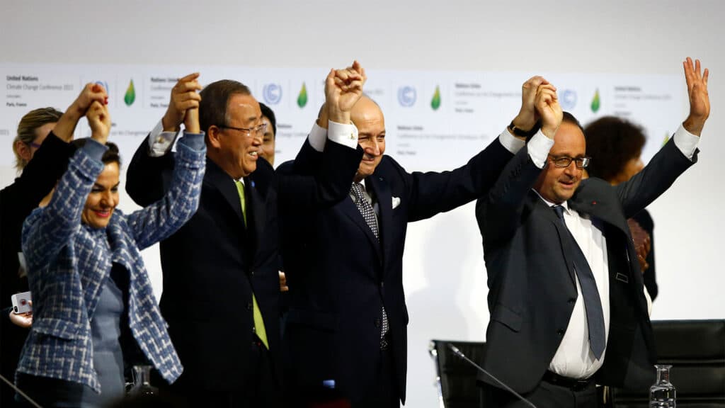 A group of people in formal attire raising their hands together in celebration at what appears to be a conference or official event.