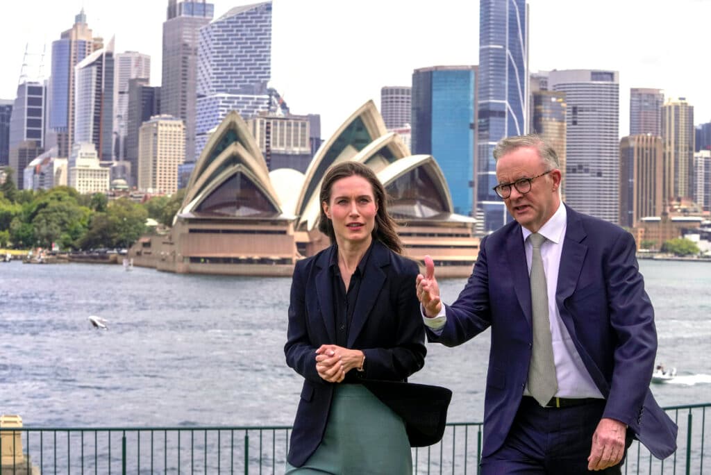 Two people in business attire walking with the Sydney Opera House and city skyline in the background.