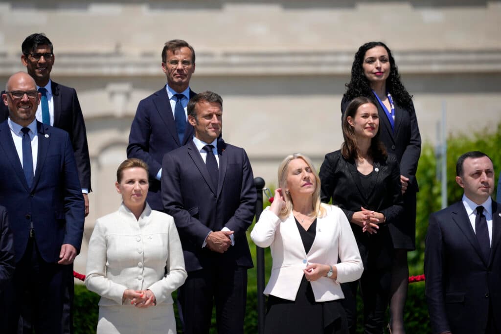 A group of nine people dressed in formal attire, standing outdoors against a blurred background, during a daylight event. They appear to be posing for a photograph.