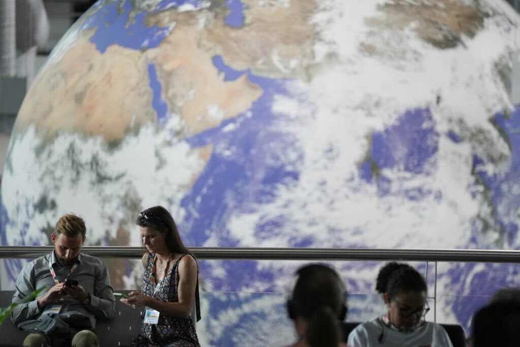 Two people sit on a bench looking at their phones in front of a large Earth globe display.