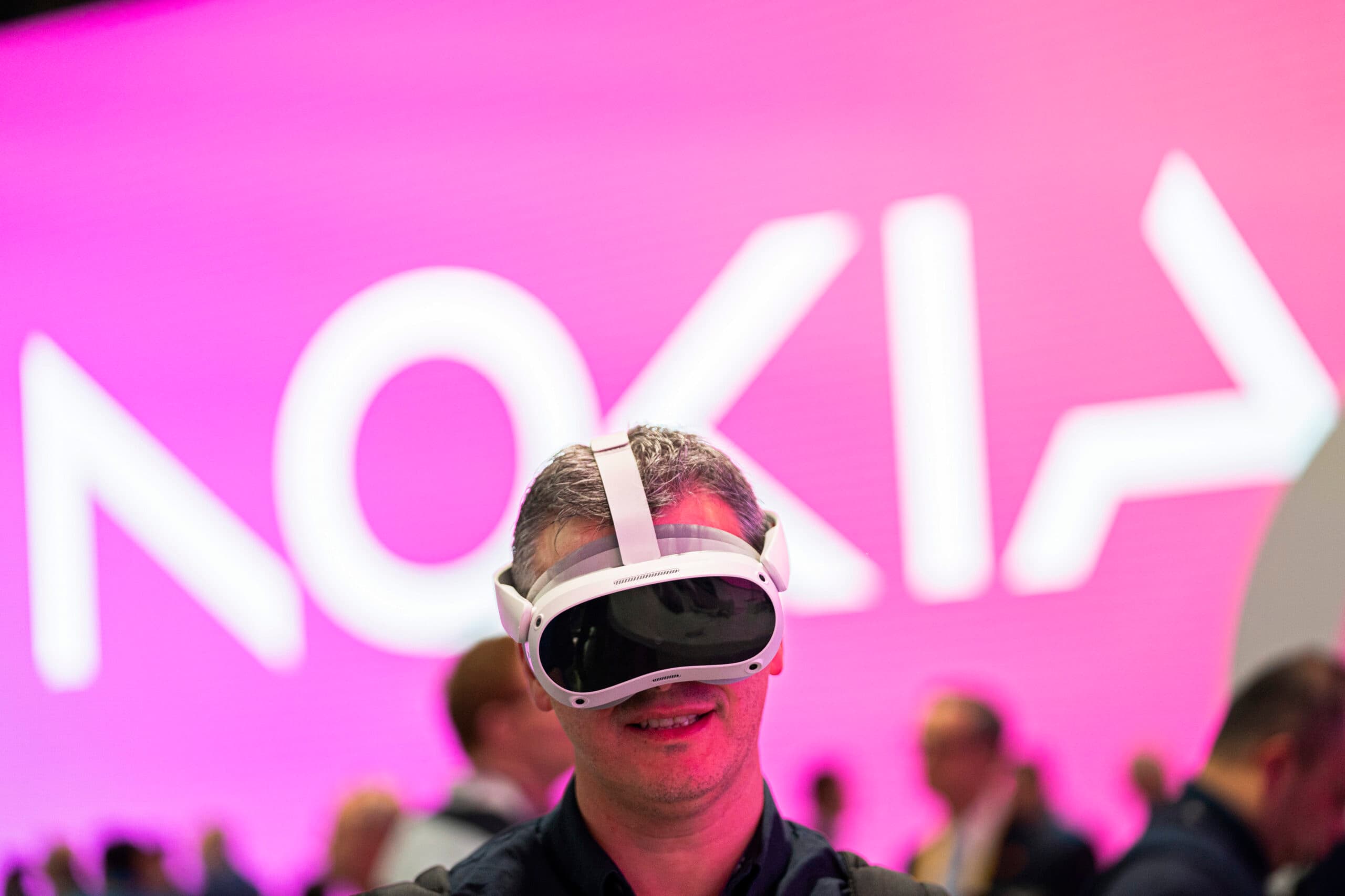 A person wearing a virtual reality headset stands in front of a large illuminated sign displaying the word "Nokia" on a pink background.