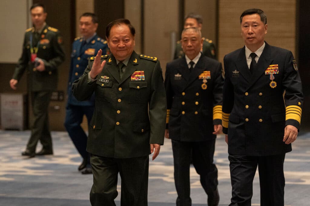 A group of military officials in uniform walking indoors, with visible medals and insignia on their attire.