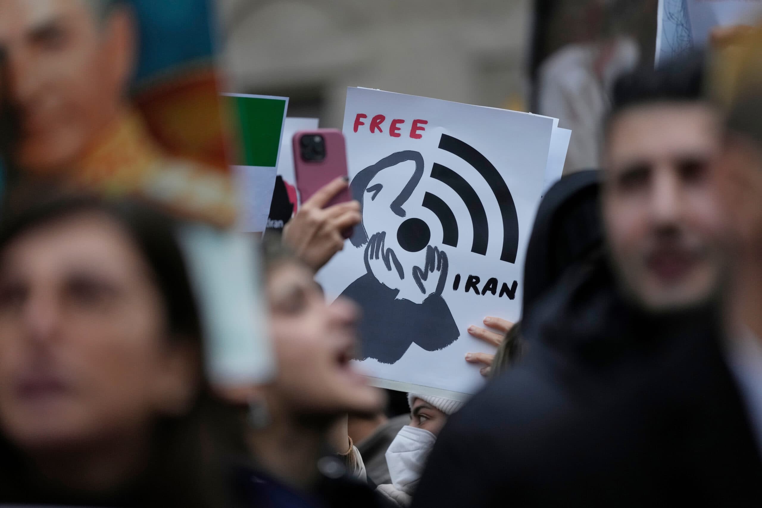 A protester holds a sign depicting a person covering their face with a Wi-Fi symbol and the words "Free Iran."