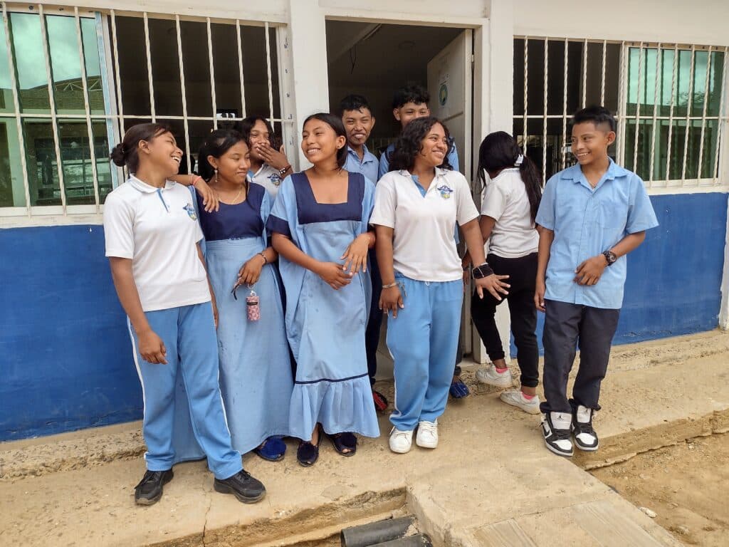 A group of nine students in blue and white uniforms standing together outside a school building, smiling and chatting.