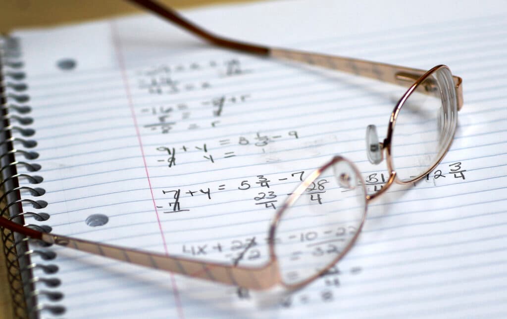 A pair of glasses resting on a spiral notebook with handwritten math equations on lined paper.
