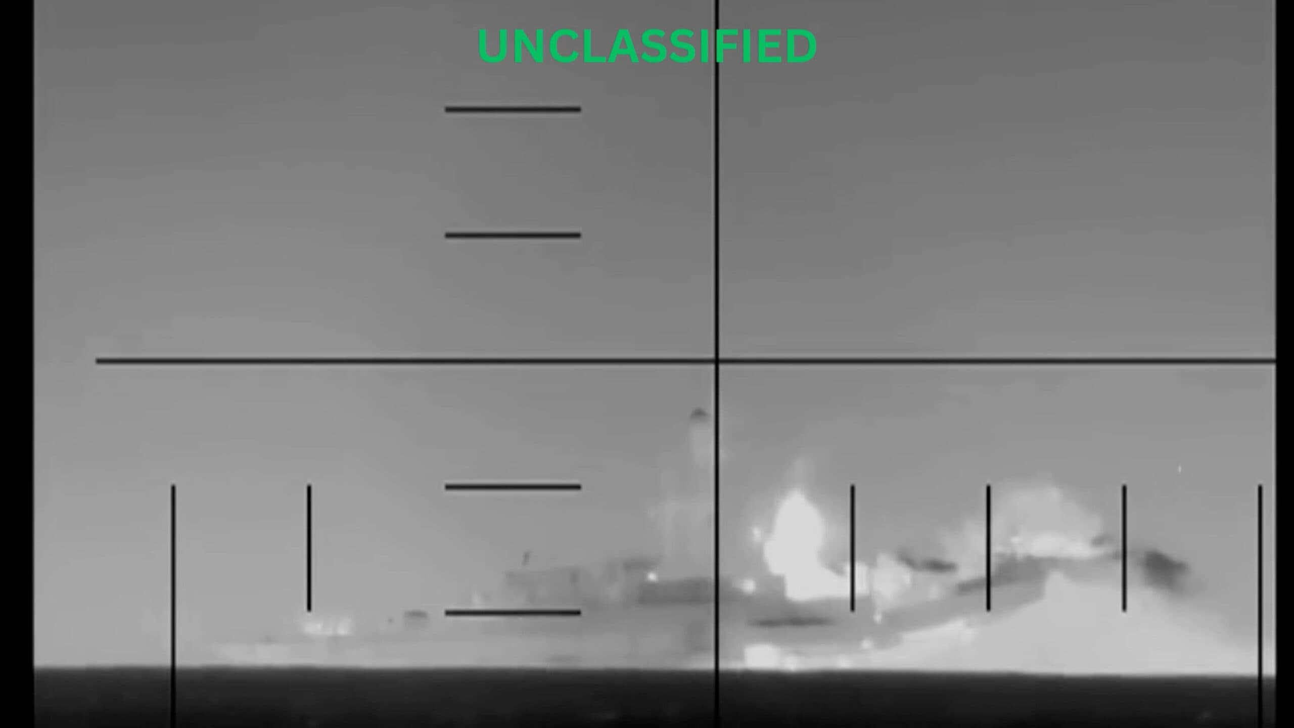Black and white thermal imaging of a ship at sea with flames and smoke visible on the right side, and crosshair overlay marked "UNCLASSIFIED" at the top.