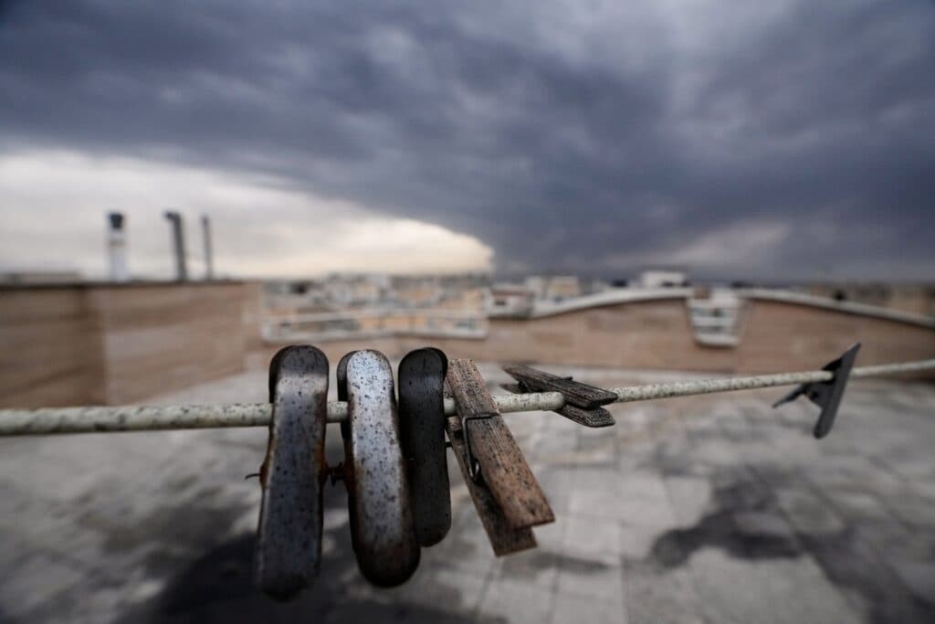 Weathered clothespins hanging on a rusty wire against a cloudy, overcast sky atop a rooftop.