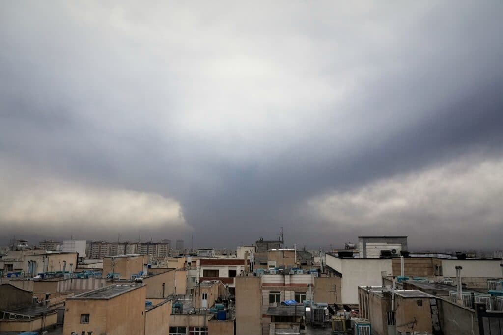 A cityscape under a cloudy sky with a dramatic, dark cloud formation above the buildings.