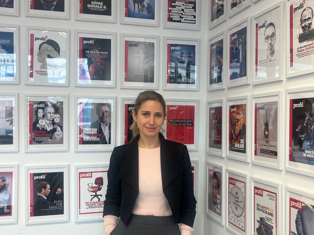 A person standing in a room with a wall displaying numerous framed magazine covers from 'profil'.