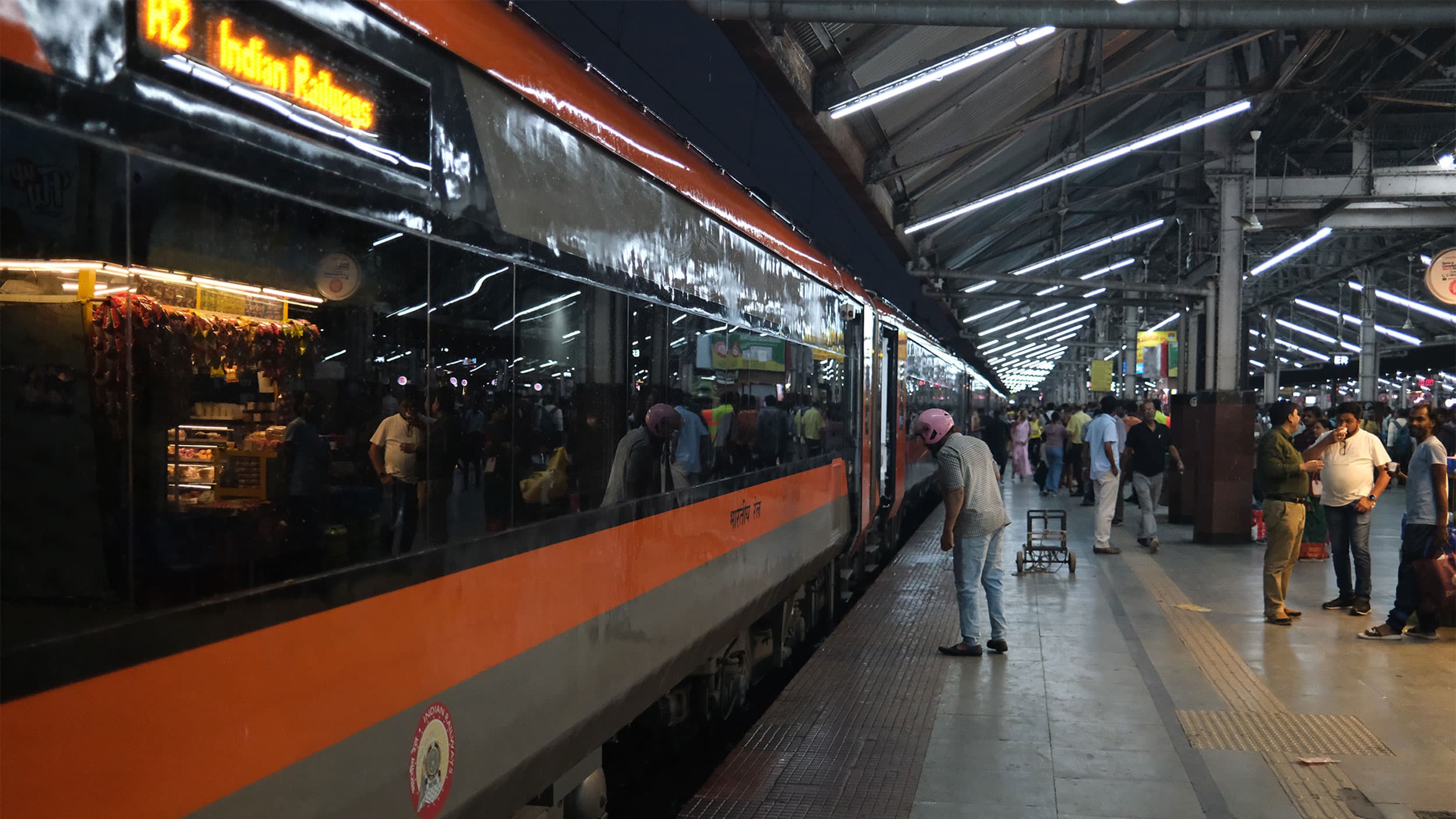 A crowded train platform with passengers boarding an orange-striped train at a well-lit station.