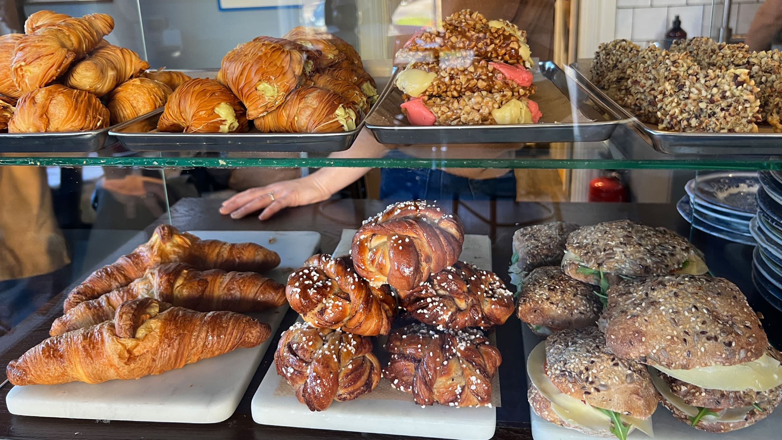 Various pastries and sandwiches displayed on trays, including croissants, filled pastries, and seeded bread rolls with cheese.