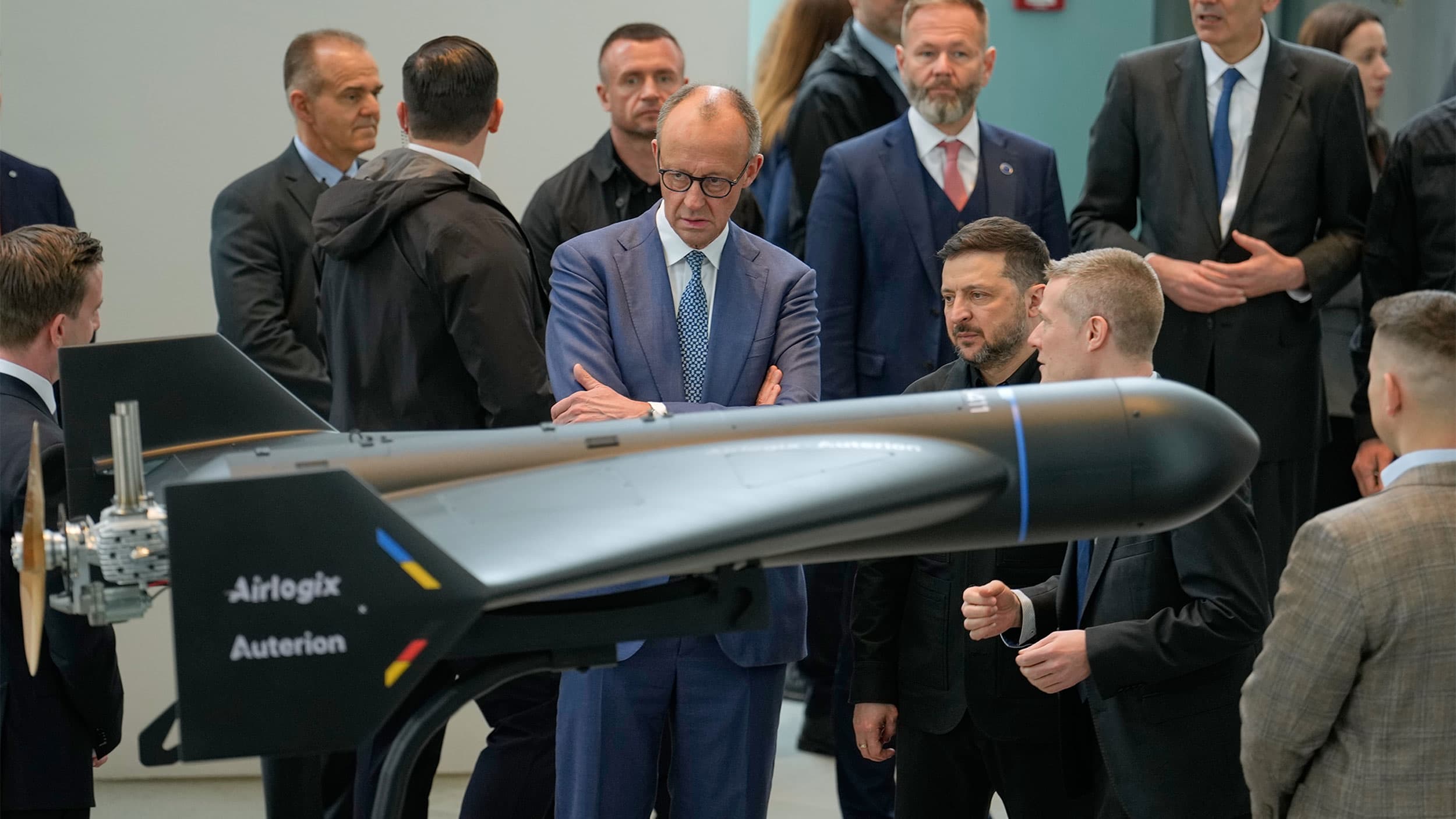 A group of people in formal attire examining a large drone model displayed indoors.