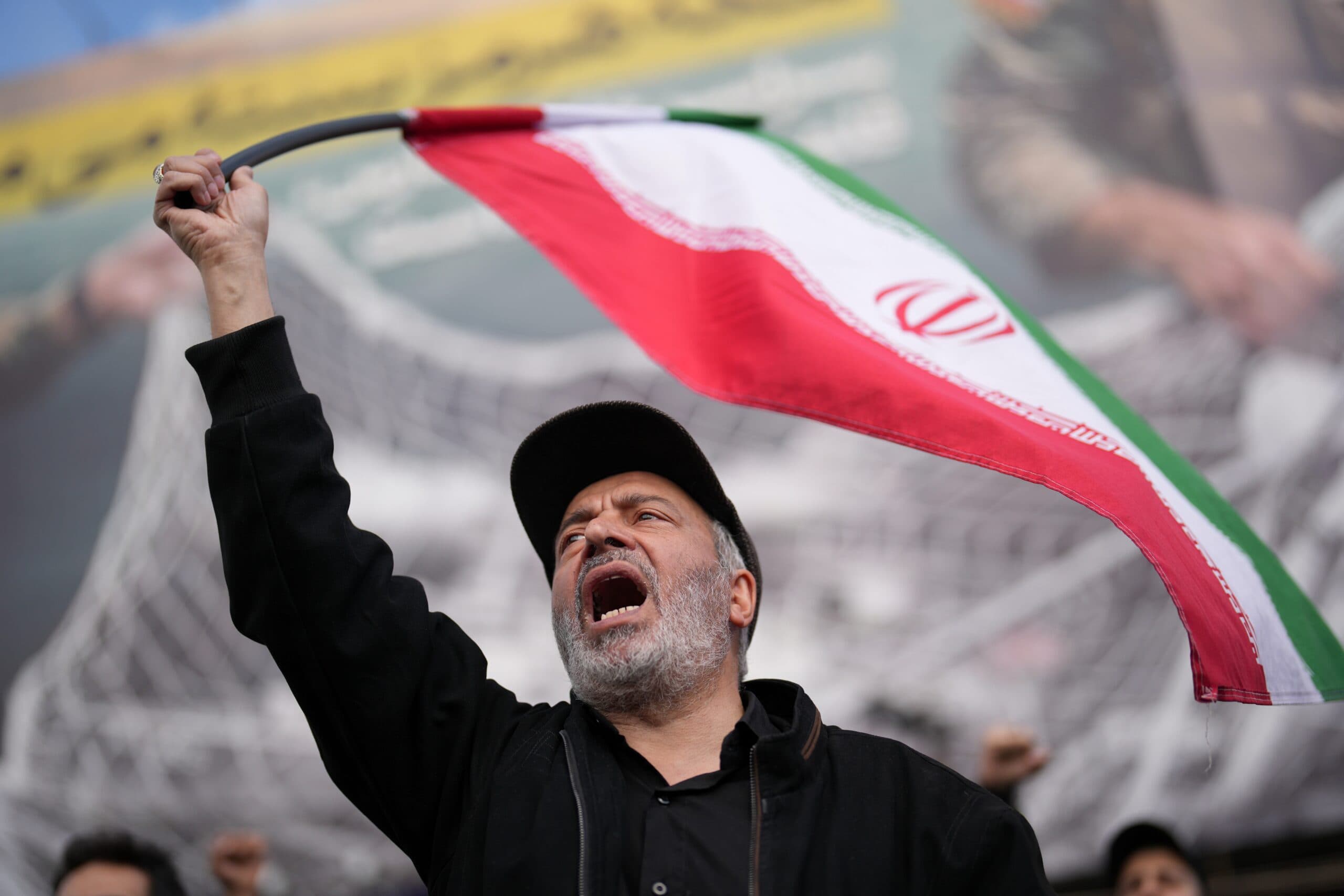 A man passionately waves an Iranian flag at a public demonstration.
