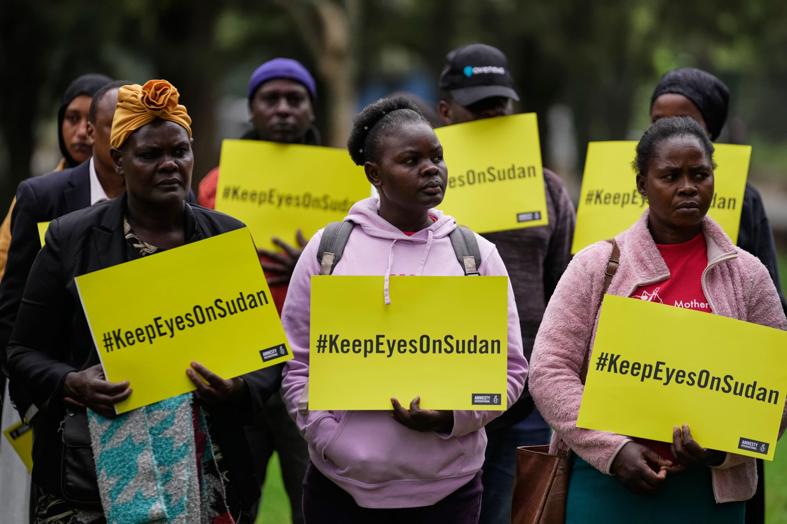 A group of people holding yellow signs that read "#KeepEyesOnSudan" during a gathering.