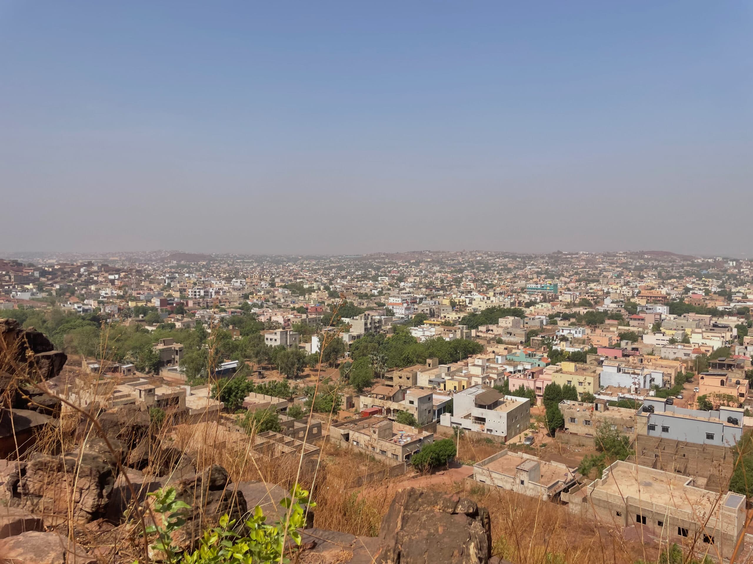 Aerial view of a sprawling cityscape under a clear sky, with numerous buildings and sparse vegetation in the foreground.