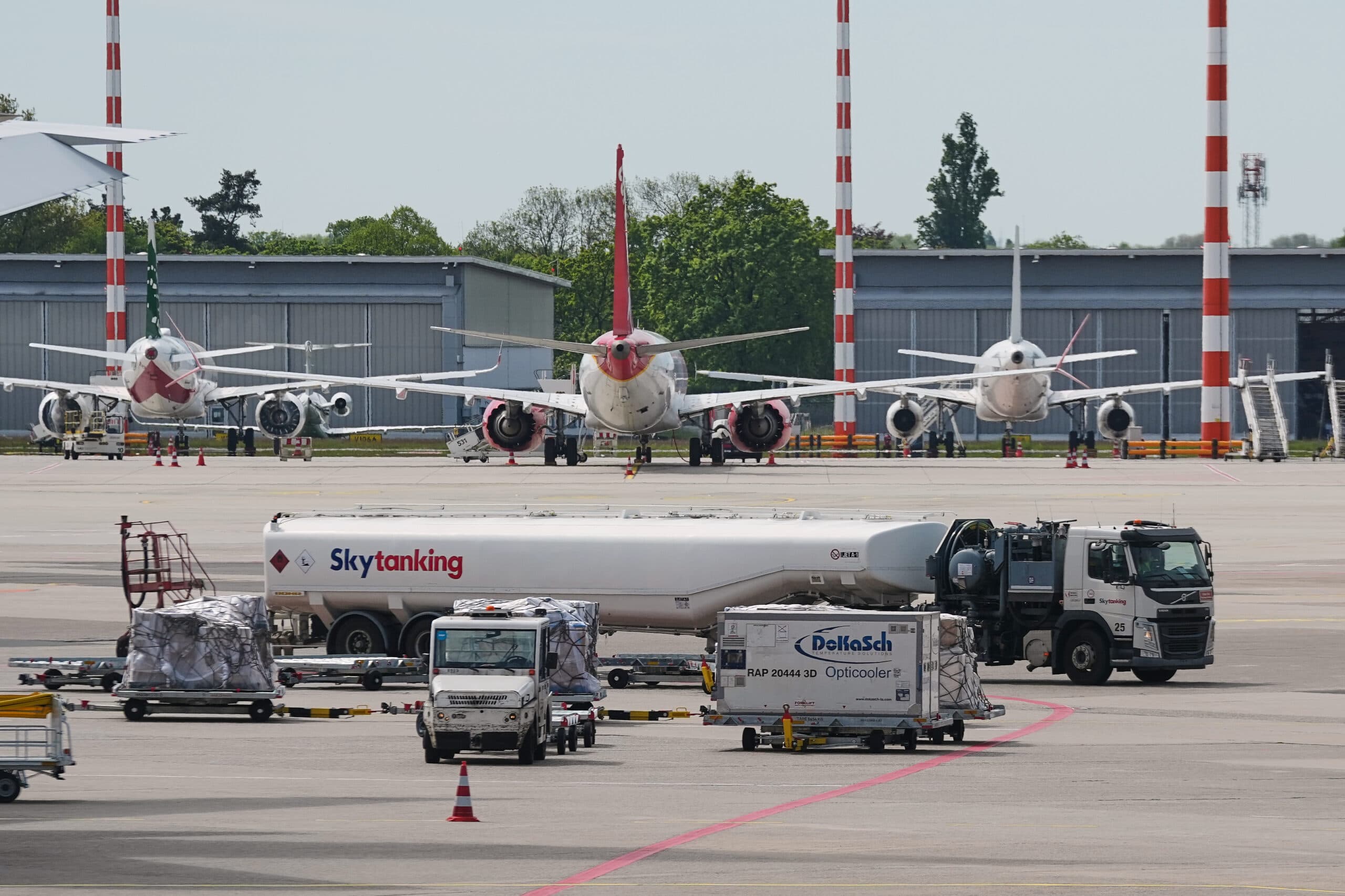 Several airplanes are parked on a tarmac near a fuel truck and service vehicles at an airport.