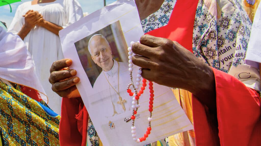 A person holds a photo of a religious leader and a red and white beaded rosary.