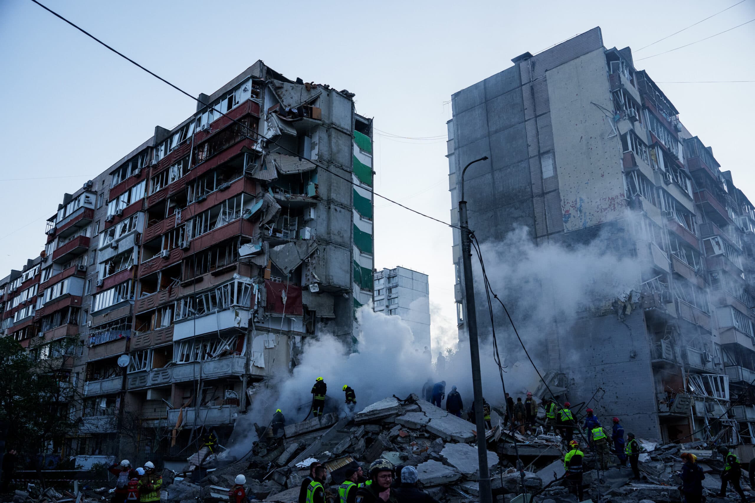 Rescue workers and smoke surround a collapsed section of a damaged residential building.
