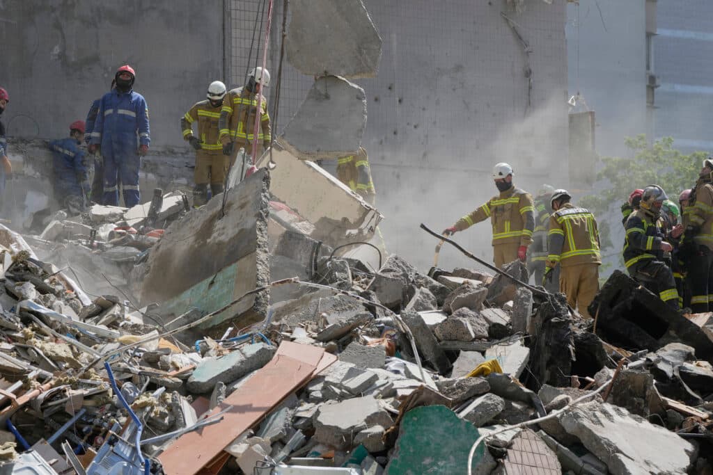 Rescue workers in helmets and uniforms search through rubble from a collapsed building.