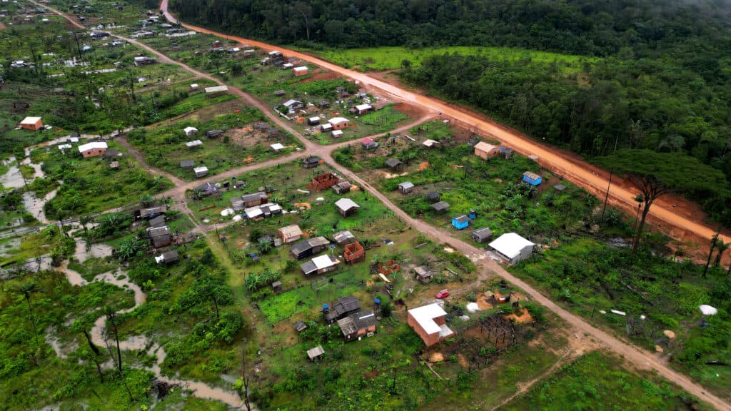Aerial view of a rural settlement with scattered houses, dirt roads, and surrounding green landscape.