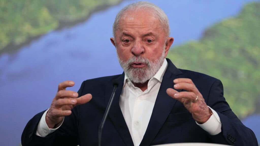 An older man with a beard speaks passionately at a podium, gesturing with both hands.