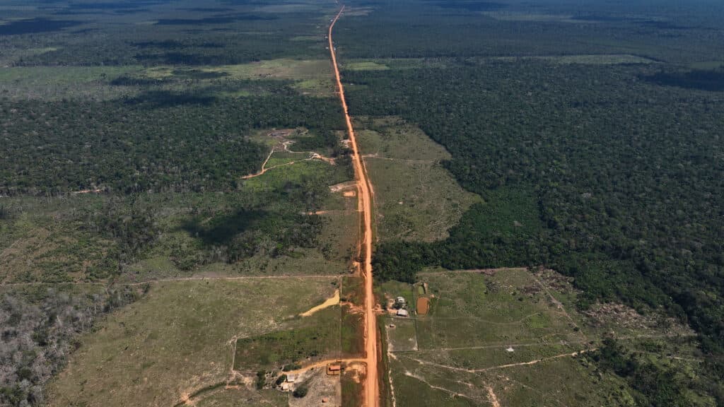 Aerial view of a long, straight dirt road cutting through a vast expanse of green forest and cleared land areas.