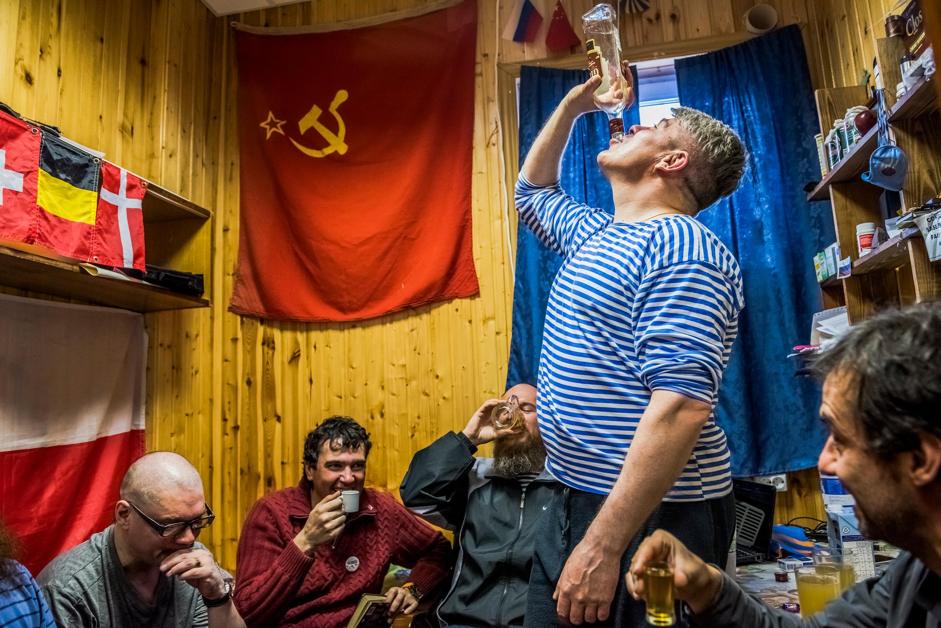 The winter expedition crew of Russian research team and a Chilean scientist drink Samagon, a homemade vodka, in a bedroom of the Bellingshausen Antarctica base; Fildes Bay, Antartica, 28 November 2015.