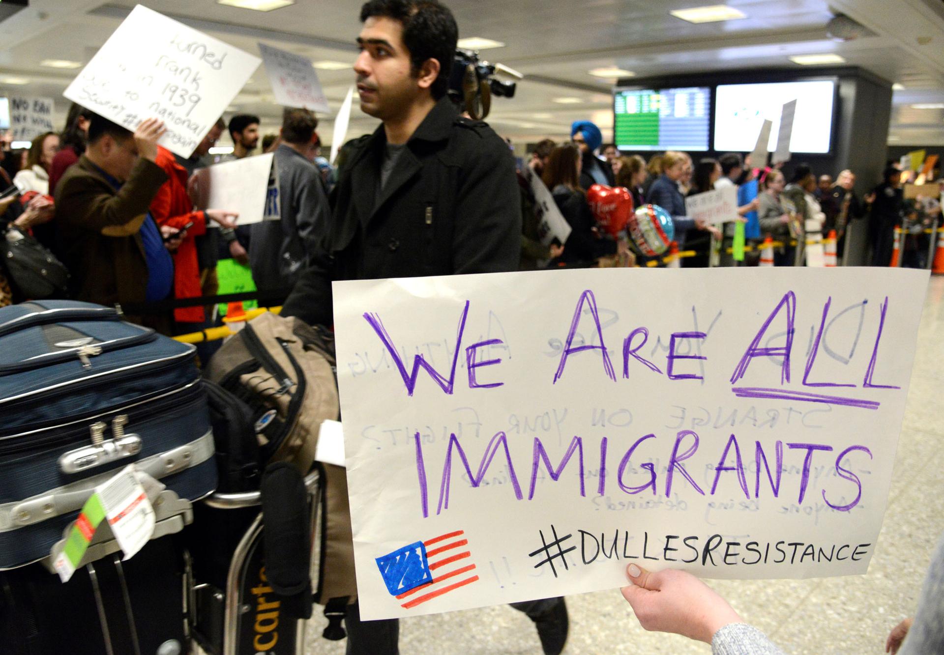 Dozens of pro-immigration demonstrators cheer and hold signs as international passengers arrive at Dulles International Airport.