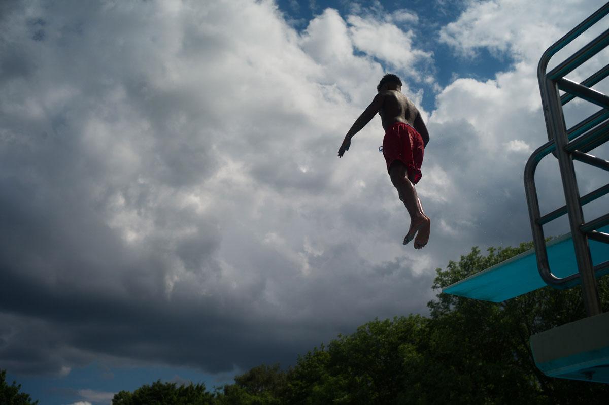 A young pool guest jumps from the diving platform of the Sommerbad Neukolln as storm clouds roll in. The director of the pool says that despite the forecasts, they are expecting a peaceful summer at the facility.