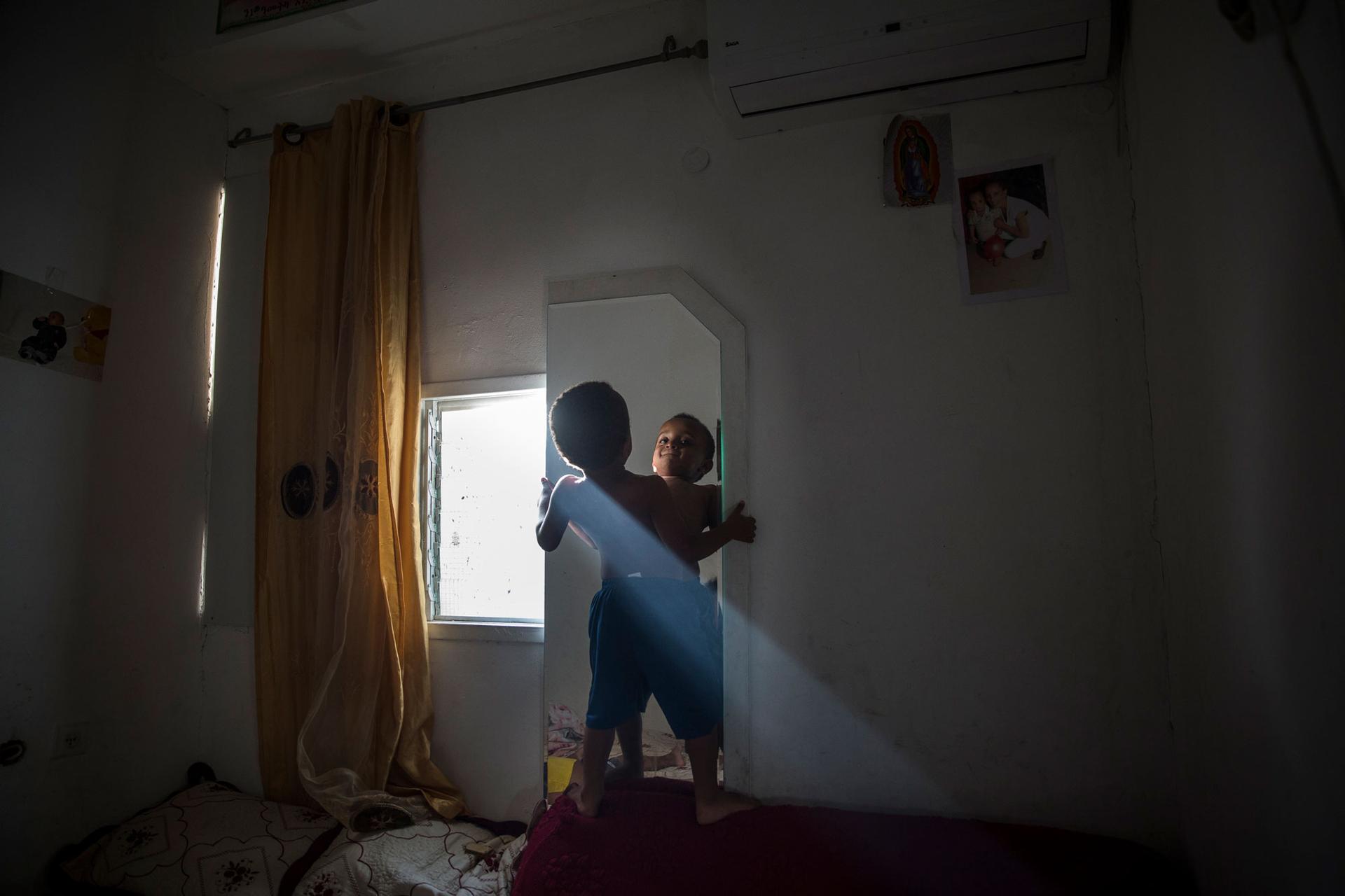 Tariki Gebru, 4, looking in the mirror in the small room he shares with his mother and younger brother in the Shapiro neighborhood of Tel Aviv.