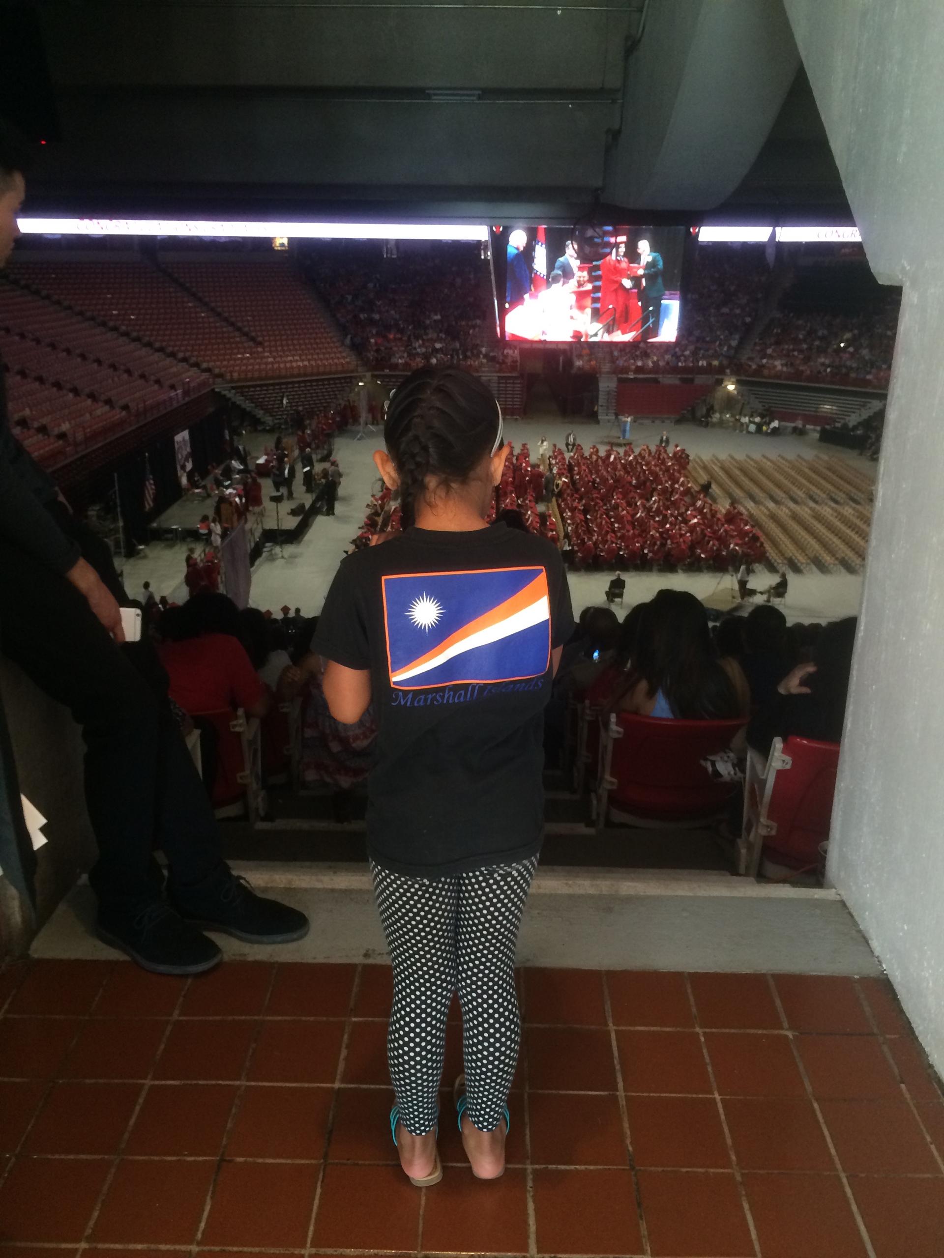 A young girl looks at graduation ceremony from above, in arena