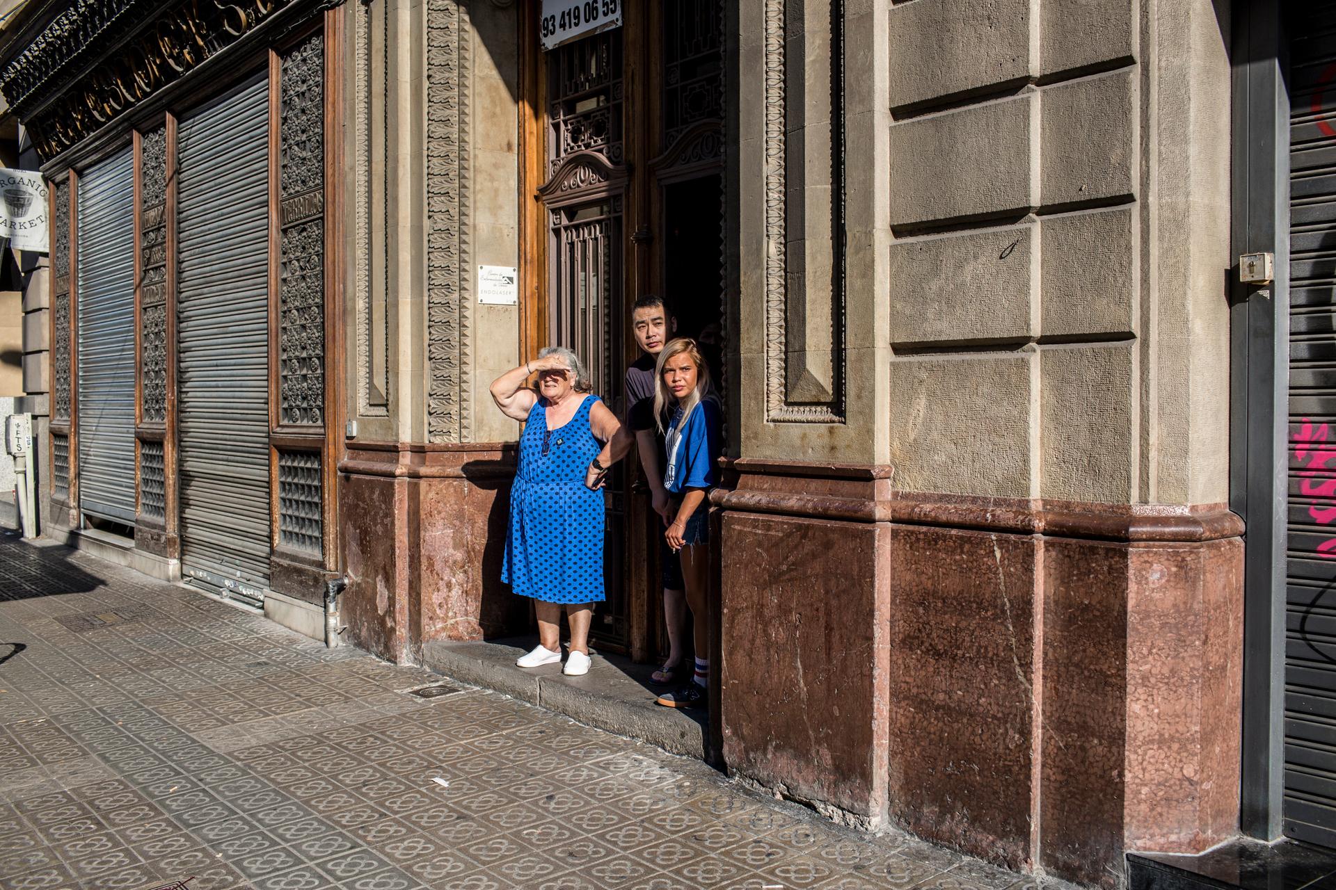 People stand on the threshold of a home on a street just outside Plaça de Catalunya as police searched for the attackers on Thursday.