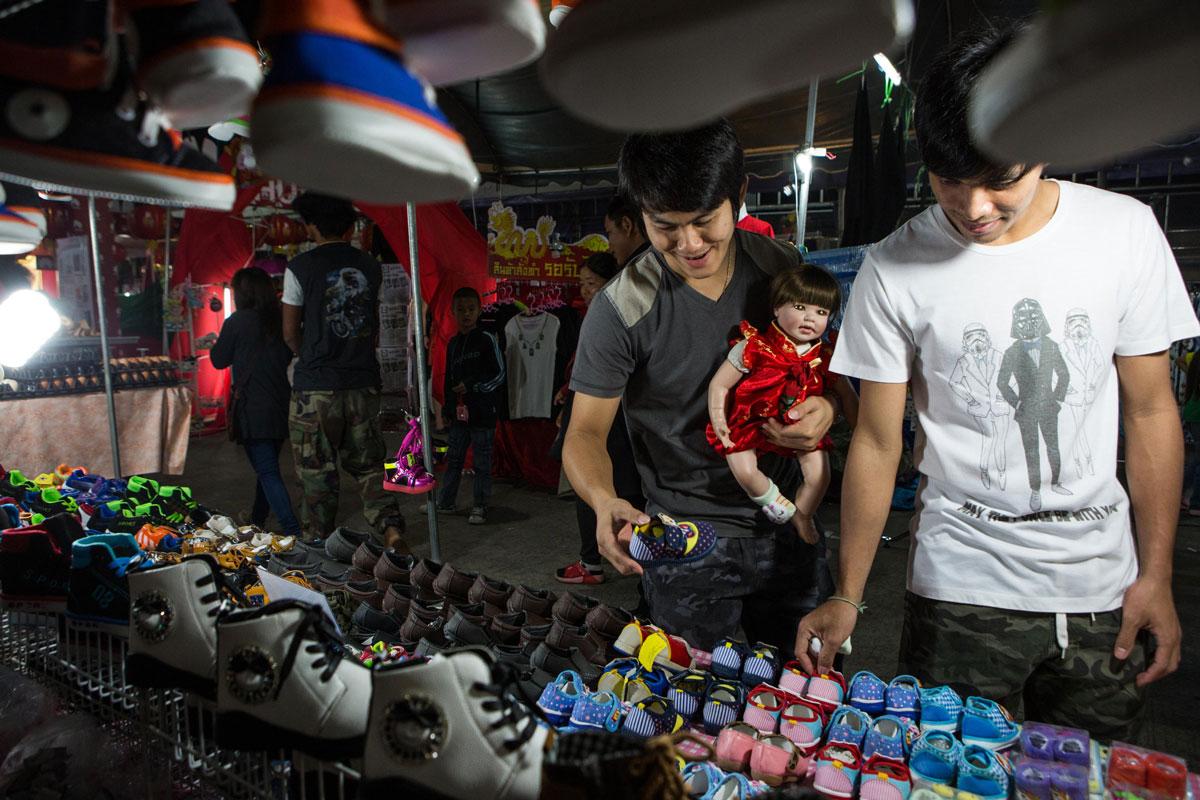 A couple shops for shoes for their doll at an outdoor market.