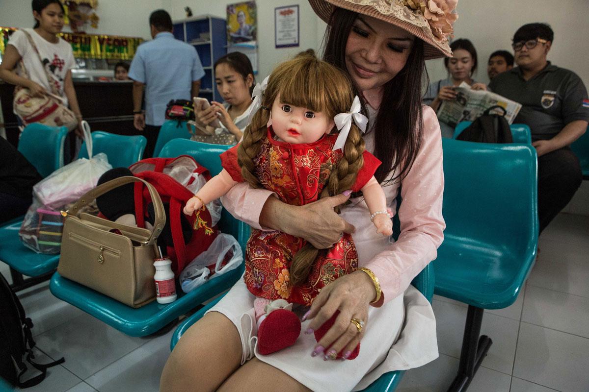 A woman waits at a bus station in Nakhon Sawan, Thailand with her luk thep named Diamond Woman.