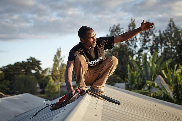An employee with M-POWER installs a solar panel on a roof near the city of Arusha, in northern Tanzania.
