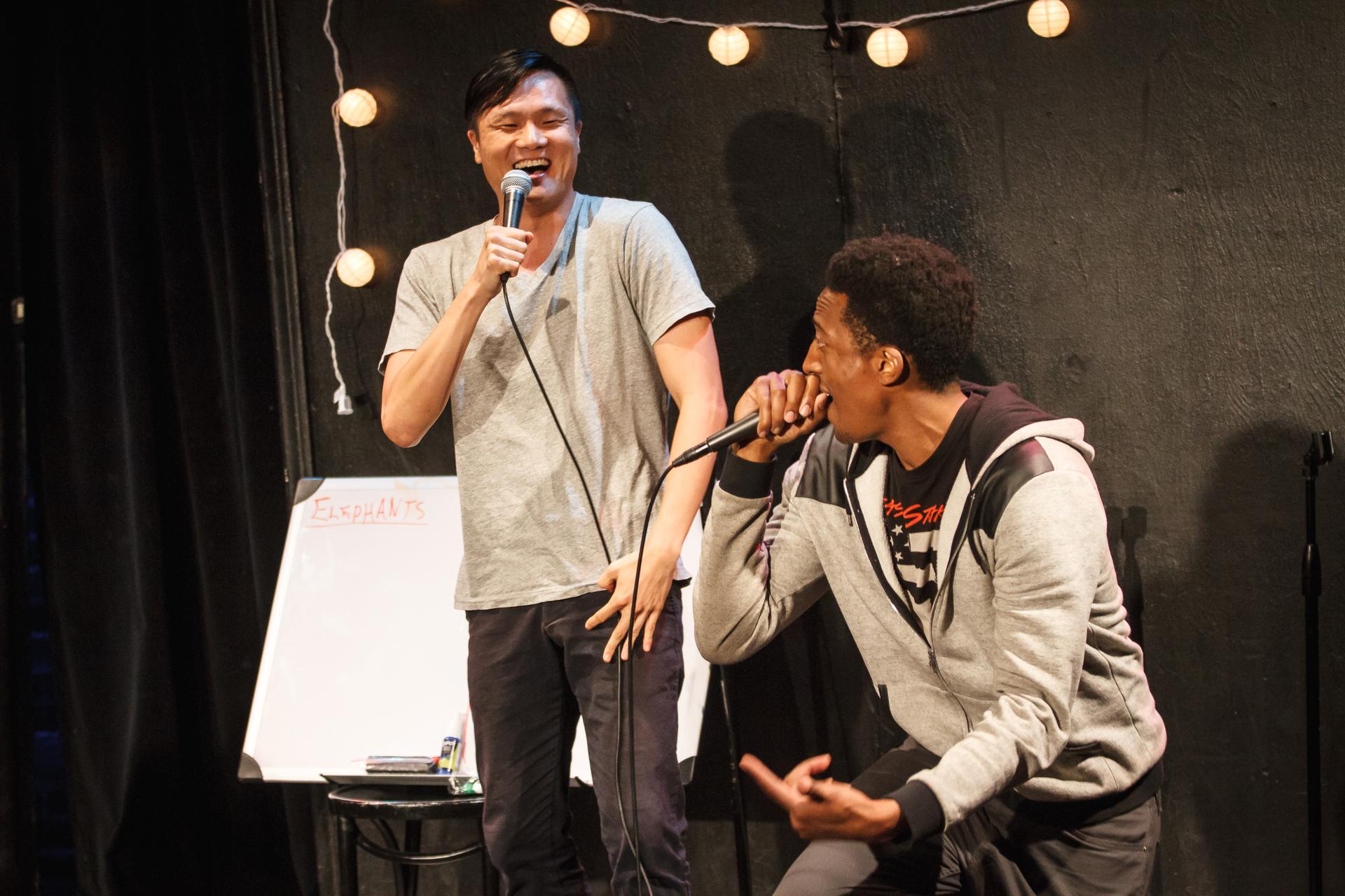 Two performers with microphones are laughing and performing their rap.