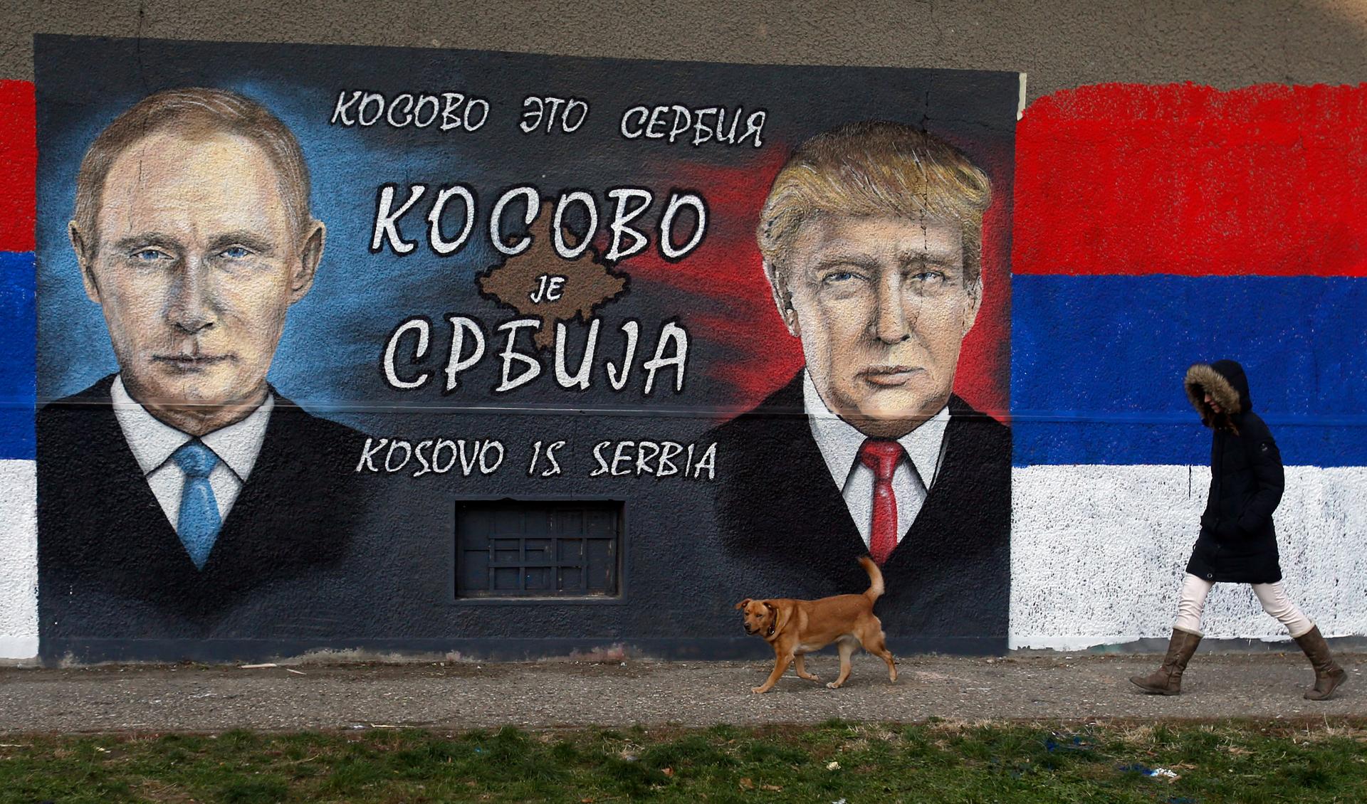 A woman passes by graffiti depicting the Russian President Vladimir Putin, left, and US President Elect Donald Trump in a suburb of Belgrade, Serbia