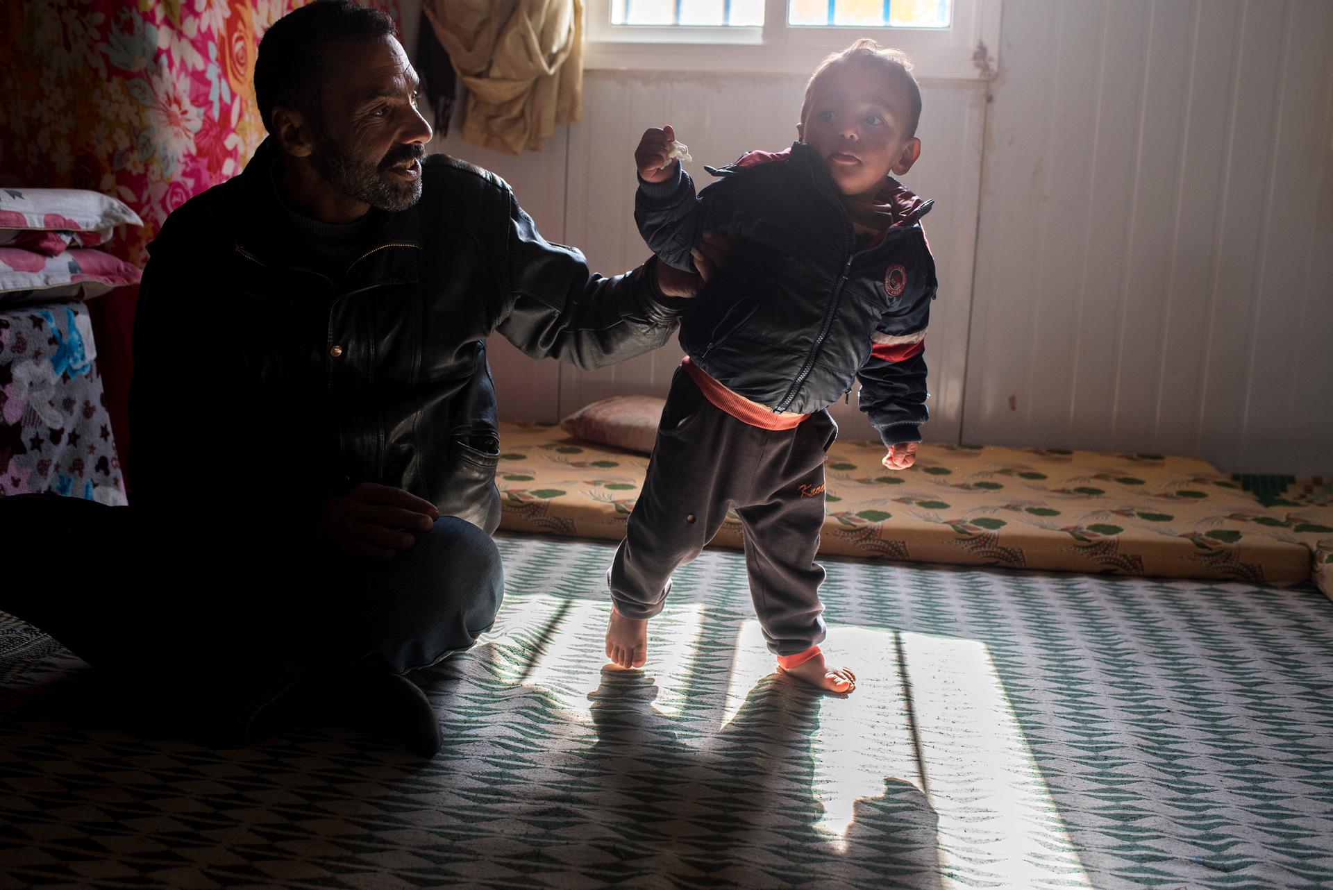 Hamdi Ahmad Laghras, 46, plays with his 1-year-old son Ibrahim in the family's metal shelter in the camp. Laghras and his wife Um Ala have had two children since fleeing Syria in 2011.