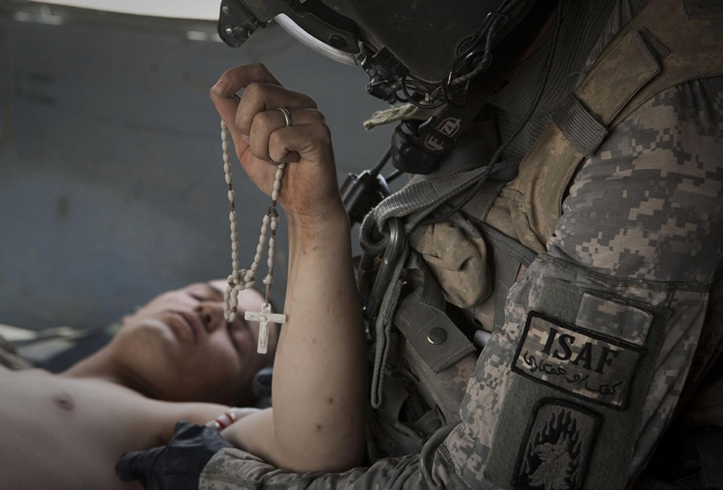 Lance Cpl. Blas Trevino of the 1st Battalion, 5th Marines, clinches his Rosary beads as he is treated by US Army flight medic Sgt. Joe Campbell after being rescued onto a medevac helicopter from the US Army's Task Force Lift 
