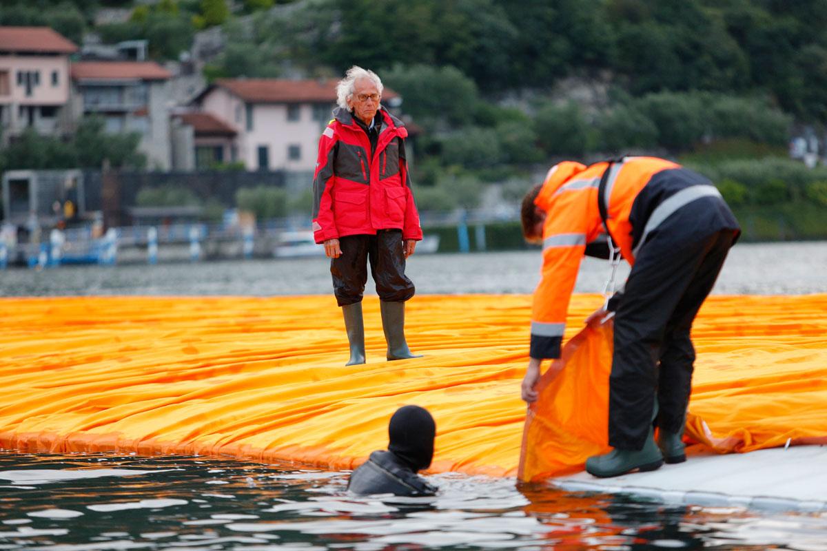 Christo watches a diver hooking a fabric panel to the side of a floating pier.