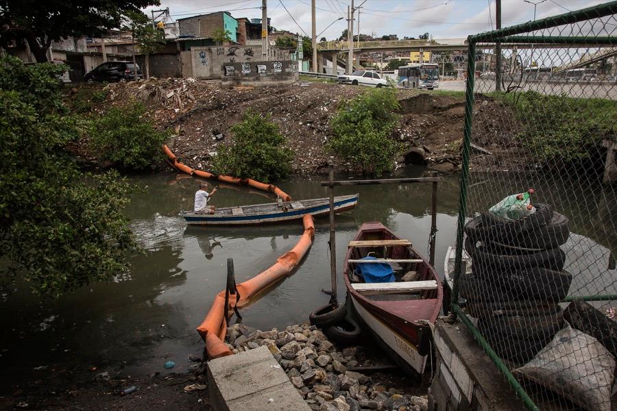 A fisherman rows through an eco-barrier that has been sliced in half on the Vila Maruí canal in the community of São Gonçalo in Rio de Janeiro.