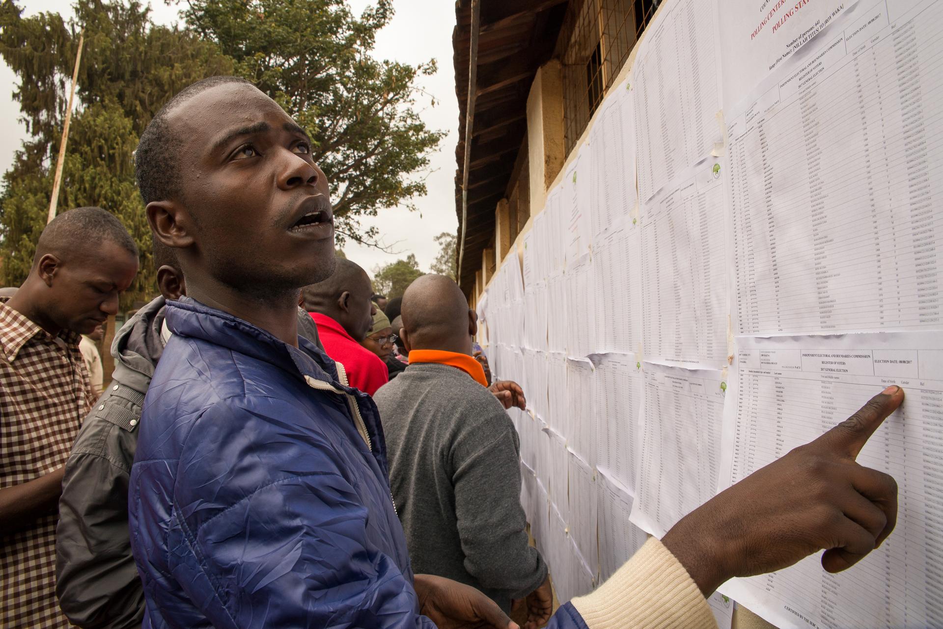 A man from an informal settlement in Nairobi searches for his name on a voter registration list at Kibera Primary School. Some voters were unable to locate their names on the registrar, forcing them to contact election officials for assistance.