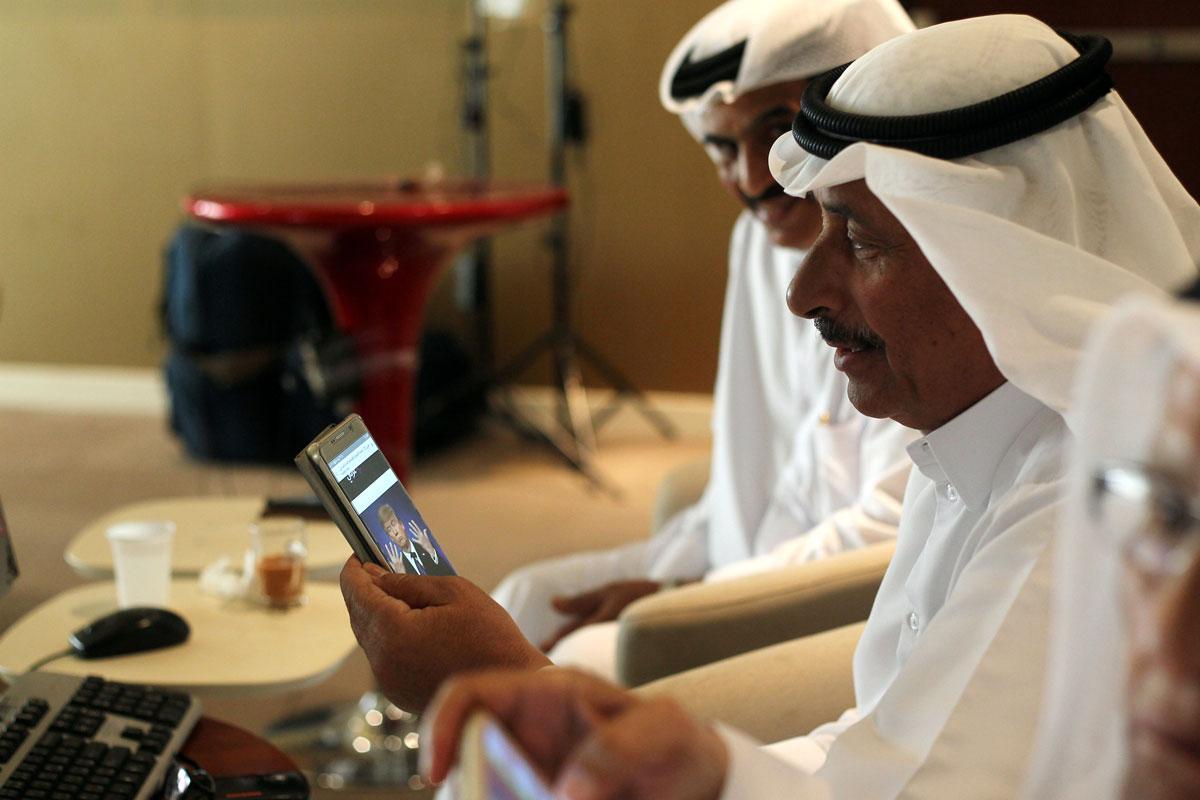 A trader uses his smartphone to follow news of the US presidential elections as he monitors a screen displaying stock information at Qatar Stock Exchange in Doha.