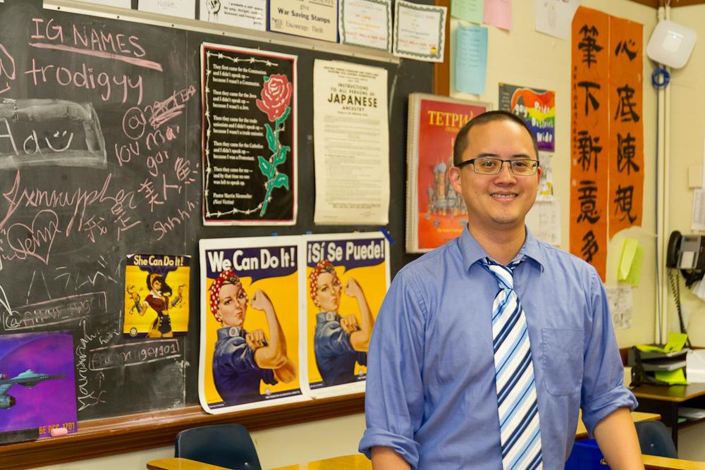 Man in front of his classroom, which has different languages on posters