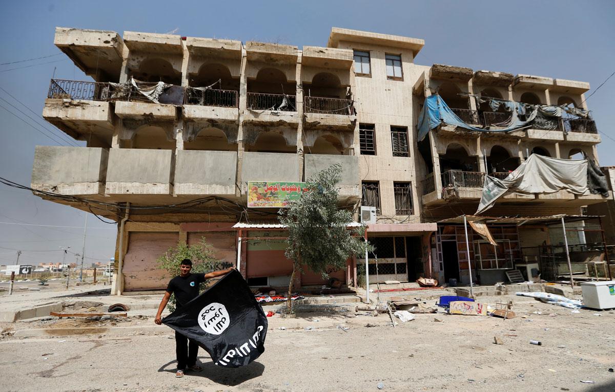 A member of the Iraqi security forces holds an ISIS flag, after pulling it down from a building, in Fallujah.