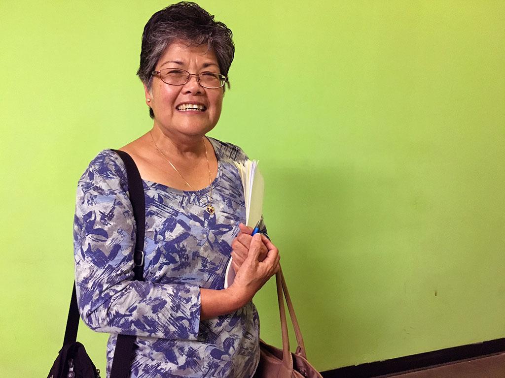 A woman holds her purse, smiles for camera, in front of green wall