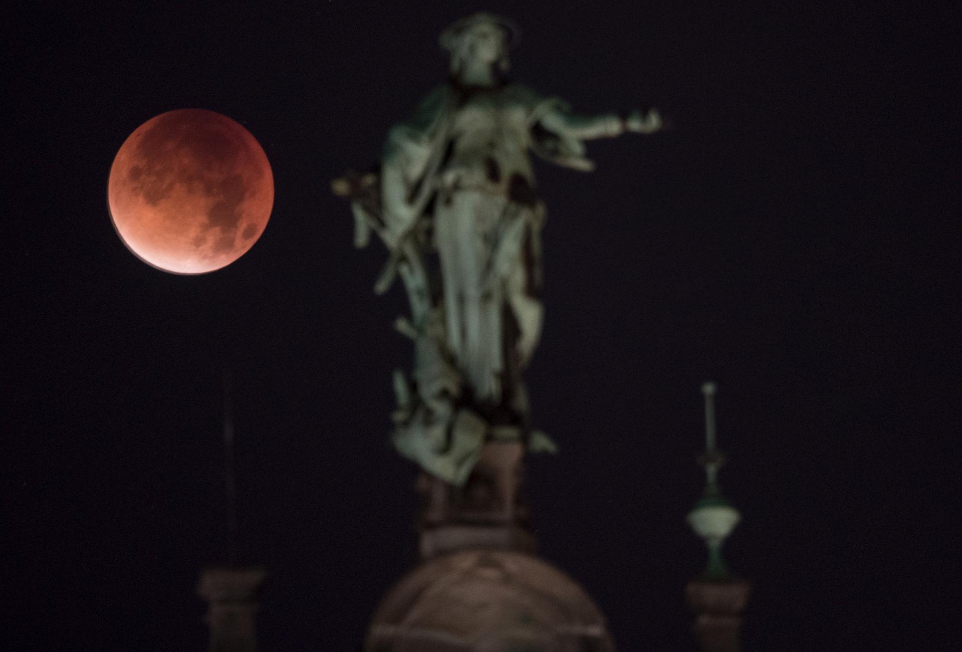 The moon, appearing in a dim red color, is covered by the Earth's shadow during a total lunar eclipse over a staute at the roof of the town hall in Hamburg, Germany.
